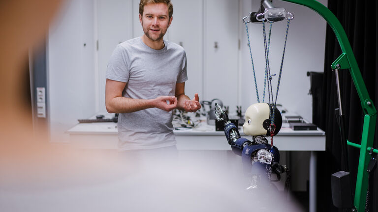 Ein Mann steht neben einem Roboter und erklärt seine Mechanismen