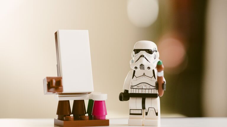 Kleine Star-Wars-Figur steht mit einem Pinsel in der Hand neben einer Leinwand