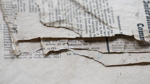 Insbesondere durch den Säurefraß wird die Zellulose abgebaut, die für die Festigkeit des Papiers verantwortlich ist. Nahaufnahme von Dokumenten, die am Rand zerfressen sind