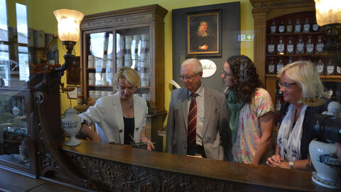 Ministerin Dorn schaut sich im Kur-Stadt-Apothekenmuseum in Bad Schwalbach mit Museumsvertretern eine Vitrine in einer historischen Apotheke an 