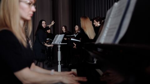 Frau am Klavier im Vordergrund, im Hintergrund sieht man eine Dirigentin