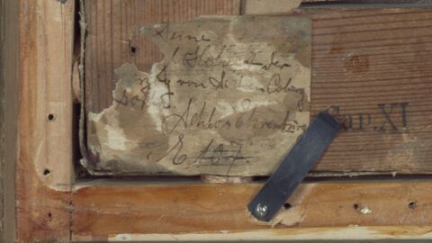 Vermutlich wurde der Zettel bei der Ausleihe des Gemäldes an die Darmstädter Jahrhundertausstellung 1914 angebracht, denn es ist im Katalog der Ausstellung bei den Porträts unter der Nummer 107 verzeichnet. Das Zeichen/der Buchstabe vor der Nummer ließ sich bisher nicht entziffern. Nahaufnahme des Klebezettels unten links