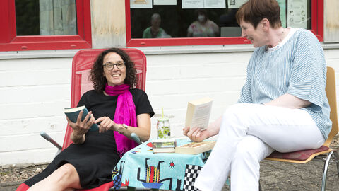 Hessens Kulturministerin Angela Dorn hat das Team der evangelischen Gemeindebücherei in Mümling-Grumbach für sein vorbildliches Engagement gewürdigt Ministerin Dorn liegt mit einem Buch im Liegestuhl, eine Mitarbeiterin der Bücherei sitzt daneben