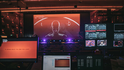 Perfomance während einer Biennale: Man sieht viele Bildschirme und einen Androidkopf auf der Bühne