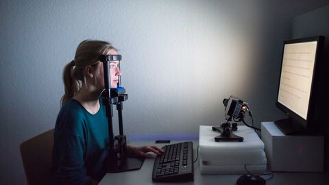 Können die Leistungen von Schülerinnen und Schülern verbessert werden, indem man das Lernen gezielt erschwert? Eine Frau sitzt vor einem Bildschirm, ihren Kopf stüzt sie auf ein Gestell, sie wird gefilmt