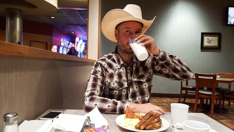 Robert-Gernhardt-Preisträger Fredy Gareis Fredy Gareis sitzt mit Cowboyhut am Tisch in einem American Diner und trinkt aus einem Glas, vor ihm steht ein halbleerer Teller mit Brotscheiben