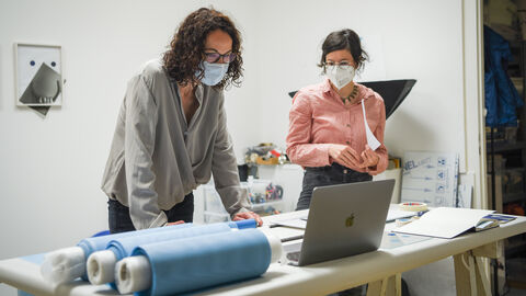 Angela Dorn steht in einem Atelier und beugt sich zu einem Computer herunter, neben ihr steht die Künstlerin