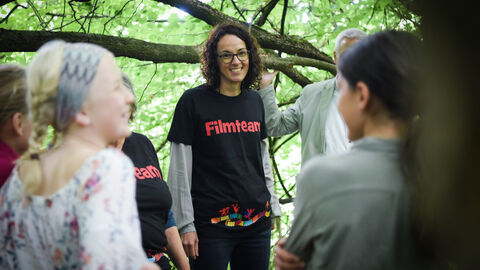 as Bulliwood-Filmmobil hat Kinder und Jugendliche eingeladen, am Wassererlebnishaus Fuldatal eine Woche lang einen eigenen Kurzfilm zu drehen Angela Dorn steht mit Jugendlichen im Wald, sie trägt ein T-Shirt, auf dem "Filmteam" steht