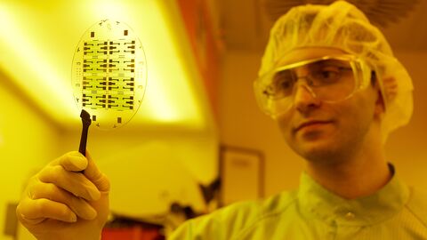 Ein Forscher im Schutzanzug hält ein Preparat mit einer Pinzette in die Kamera