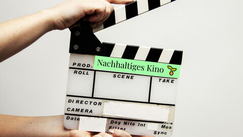 Referenzkinos erhalten Unterstützung und Beratung Eine Hand hält eine Filmklappe, auf der "Nachhaltiges Kino" steht
