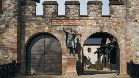 Das Römerkastell Saalburg Blick auf das Eingangstor des Römerkastells Saalburg. Zu sehen ist eine steinerne Mauer und eine römische Skulptur, die ihren Arm zum Gruß hebt