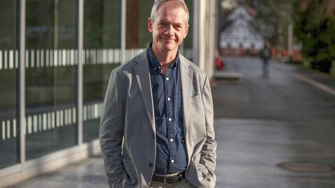 Stefan G. Hofmann wechselt zur Philipps-Universität Marburg Prof. Dr. Hofmann steht vor einem Universitäsgebäude. Er hat kurze graue Haare, trägt ein graues Jackett und ein blaues Hemd und lächelt in die Kamera, die Hände in den Hosentaschen