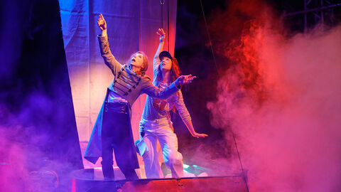 Szene aus "Am Hafen mit Vogel" Szene aus "Am Hafen mit Vogel": Zwei Schauspielerinnen auf der Bühne, umgeben von bunten Nebel, zeigen gen Himmel