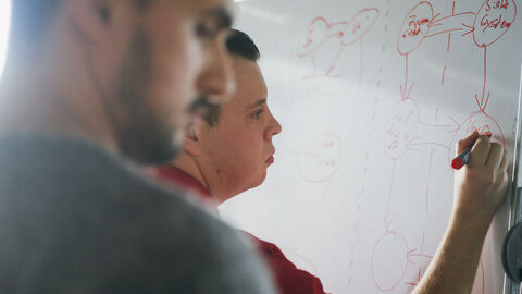 Zwei Männer schreiben an ein Whiteboard Zwei Männer schreiben an ein Whiteboard