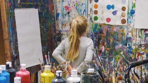 . Wem bereits als Kind die Möglichkeit gegeben wird, die Sprache der Kunst zu entschlüsseln, der wird sein ganzes Leben lang durch die Künste immer wieder neue Welten entdecken  Mädchen steht in einem Atelier und schaut auf ein Plakat mit Farbmischungen; die Leinwand ist noch leer