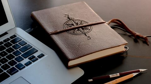 Zur Vertiefung der interkulturellen Kontakte wurde 2005 das Hessische Literaturstipendium ins Leben gerufen Ein Laptop auf einem Tisch, daneben liegt ein in Leder eingeschlagenes Buch mit einem Kompass auf dem Buchtitel