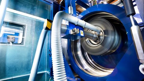 Anlage im Fraunhofer LBF Wissenschaftliche Anlage beim Fraunhofer LBF: Man sieht ein großes balues Gerät mit runder Öffnung, hinter einer Scheibe beobachtet ein Mitarbeiter das Geschehen