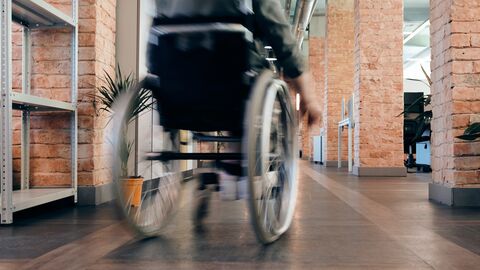 Wer eine Behinderung hat oder mit einer chronischen Erkrankung lebt, stellt besondere Anforderungen an sein Studium Mensch im Rollstuhl in Bewegungsunschärfe, der einen Flur entlangfährt