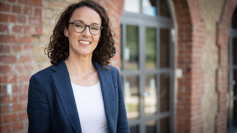 Angela Dorn vor einer Backsteinwand mit großem Fenster