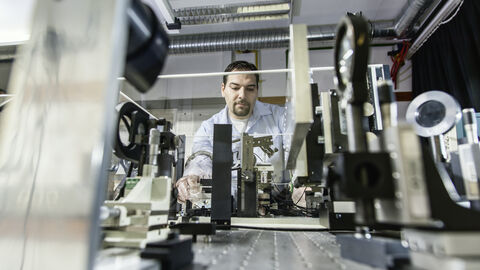 Ein Mann arbeitet an einem Tisch, man sieht ihn zwischen wissenschaftlichen Geräten