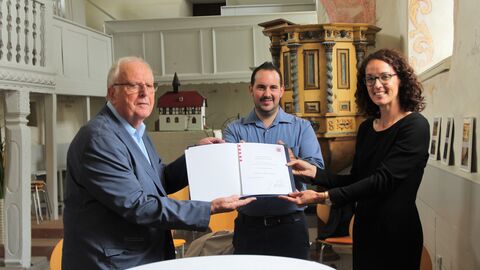 Angela Dorn steht mit Vereinsvertretern in der Kirche und überreicht ihnen eine Urkunde