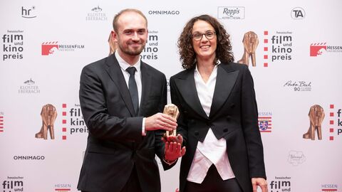 Der mit 7.500 Euro dotierte Newcomerpreis, über dessen Vergabe die Kunst- und Kulturministerin entscheidet, geht an Aliaksei Paluyan Ministerin Dorn und Aliaksei Paluyan stehen nebeneinander und halten die Filmpreis-Trophäe in die Kamera