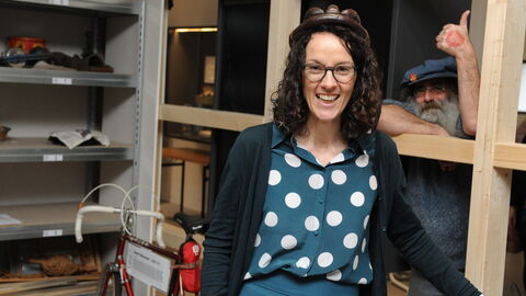 Im RadWerk Hanau kommen alle auf ihre Kosten, deren Herzen für Zweiräder schlagen Ministerin Dorn trägt einen antiken Fahrradhelm und lächelt in die Kamera, im Hintergrund zeigt der Museumsleiter den Daumen nach oben