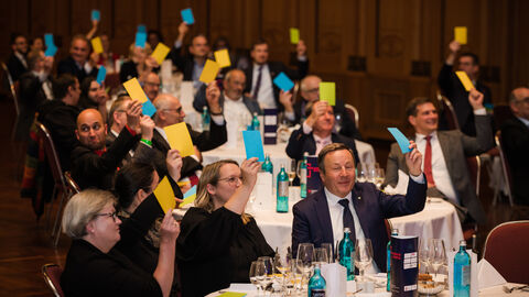 Gäste des Festaktes halten verschiedenenfarbige Karten in die Luft