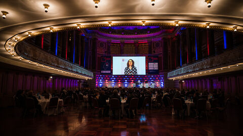Blick in den Festsaal; auf einer großen Leinwand ist ein Video mit Ministerin Dorn zu sehen