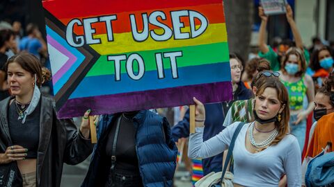 "Get used to it" - "Gewöhnt euch dran" - fordern diese queeren Aktivist*innen Queere Aktivist*innen halten ein regenbogenfarbenes Schild in der Hand, auf dem "Get used to it" ("Gewöhnt euch dran") steht