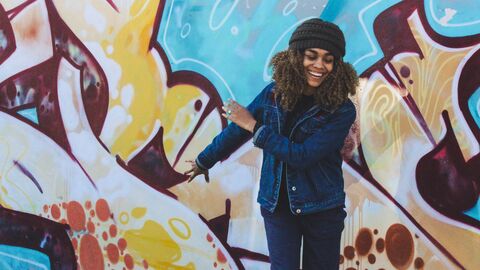 Eine junge Frau steht lächelnd vor einer Graffitiwand