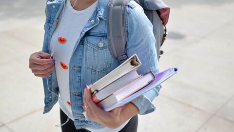 Eine Person mit Büchern und Rucksack, das Gesicht sieht man nicht