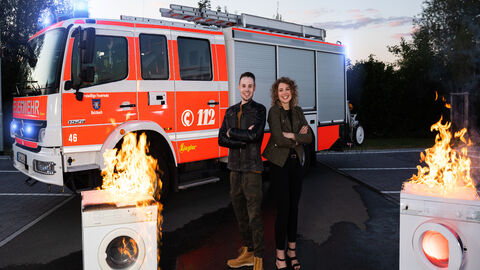 Fabian Goedert und Sophia Reiter haben ein Brandschutzsystem für elektrische Geräte zum Patent angemeldet Fabian Goedert und Sophia Reiter stehen vor einem Feuerwehrauto, neben ihnen brennen Waschmaschinen