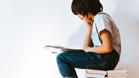 Ein Kind sitzt lesend auf einem Bücherstapel