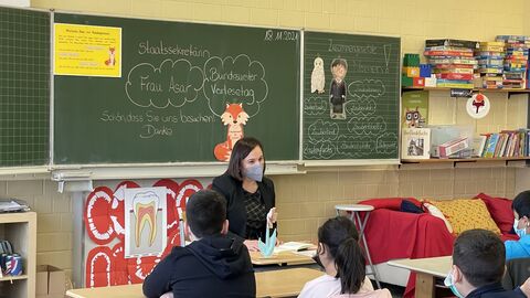 Staatssekretärin Asar sitzt vor der Tafel im Klassenraum und liest Schulkindern vor