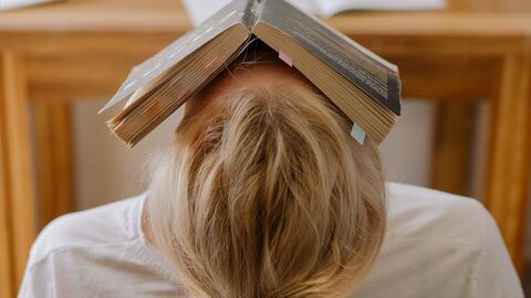 Keine Panik, es gibt wieder Entlastungen für Studierende in der Pandemie. Eine Person lehnt sich im Stuhl zurück und hat ein Buch auf dem Gesicht liegen