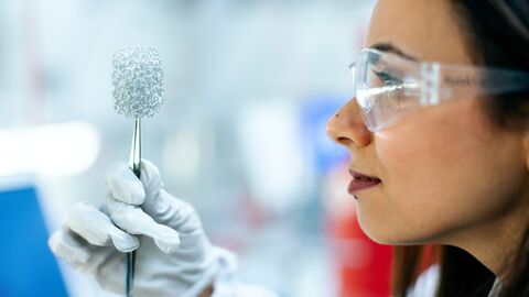 Eine Forscherin hält mit einer Pinzette einen silbernen Gegenstand
