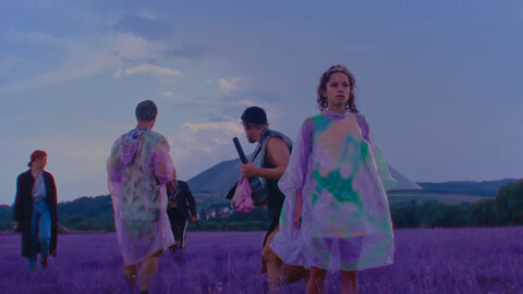 Szene aus "YOUTH TOPIA" Szene aus "YOUTH TOPIA": Jugendliche in bunten Umhängen stehen auf einem Feld