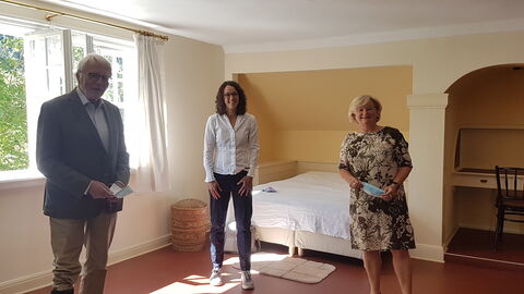 Ministerin Dorn steht mit Ludwig Rinn und Dr. Erika Schellenberger-Diederich vom Verein "Zwei Raben" in einem Zimmer des Otto-Ubbelohde-Haus 