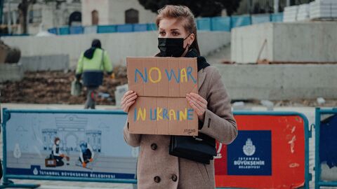 Das Hessische Ministerium für Wissenschaft und Kunst und die hessischen Hoch-schulen verurteilen gemeinsam den völkerrechtswidrigen Angriffskrieg Russlands gegen die Ukraine.  Eine Frau hält auf einer Demo ein Schild in die Hand auf dem in gelbblauen Buchstaben "No war in Ukraine" (Kein Krieg in der Ukraine) steht.