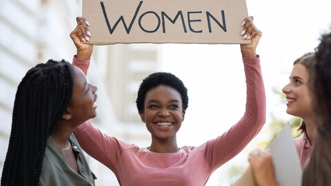 Eine Frau hält ein Schild hoch, auf dem "Women" ("Frauen") steht, sie ist umringt von weiteren Frauen