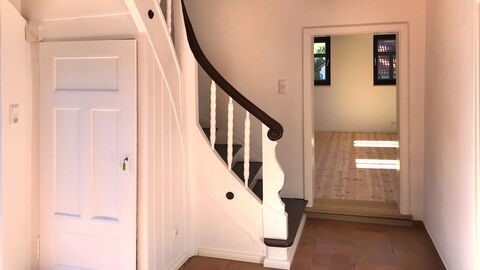 Innenansicht der sanierten Dorfschule in Herleshausen Innenansicht der sanierten Dorfschule in Herleshausen: Man sieht eine geschwungene Treppe in einer Holzdiele, unter der Treppe ist eine Tür