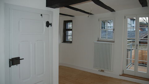 Blick in den sanierten Innenraum im Fachwerkhaus in der Marburger Kappesgasse mit freigelegten Fachwerkbalken an der Decke, weißen Wänden, hellem Holzfußboden