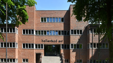 Der erste Preis beim Hessischen Denkmalschutzpreis 2022 in der Kategorie "Transformatives Bauen" ehrte Marc Köhler, Thomas Meyer und Keivan Karampour von Karampour + Meyer Architekten PartmbB. Sie haben das ehemalige Hallenbad Ost in Kassel zu einem Ort für Veranstaltungen, Büros und Praxen umgestaltet. Das ehemalige Hallenbad Kassel Ost von außen: Ein rot gehaltener Backsteinbau