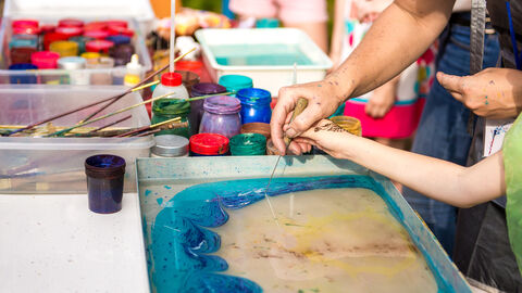 Eine Erwachsenenhand führt eine Kinderhand bei der Erstellung eines Bildes