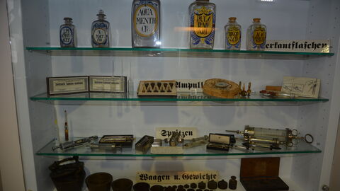 Vitrine mit Apothekerfläschchen, Ampullen, Spritzen und Waagen