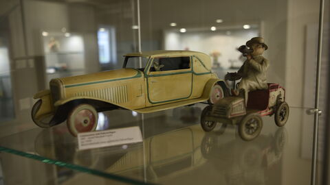 Ausstellungsstücke im Waldecke Spielzeugmuseum: Zwei Autominiaturen, eine gelbe lange Limousine und ein Männchen, das auf einem antiken Automobil sitzt und in ein Horn stößt