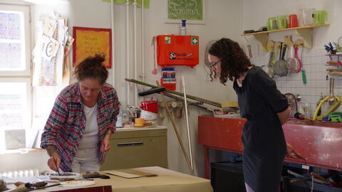 Ministerin Dorn schaut sich in der Werkstatt der Propstei Johannesberg ein, wie eine Mitarbeiterin Farbe auf einen Gegenstand aufträgt.