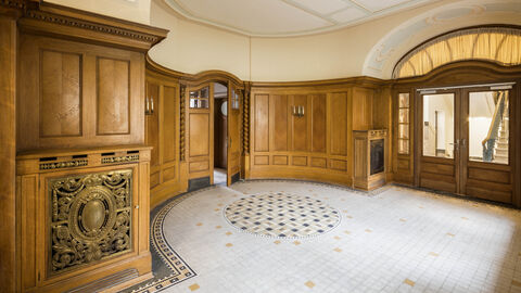 Blick in die Eingangshalle des Pressehauses Wiesbaden; die Wände sind hölzern getäfelt, der Boden weiß gefliest mit Ornamenten