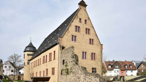 Das Solmser Schloss von außen, ein spitz zulaufender, cremefarbener Bau mit spitzem Dach und einem Rest historischer Mauer